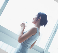早朝に窓際で水を飲んでいる女性